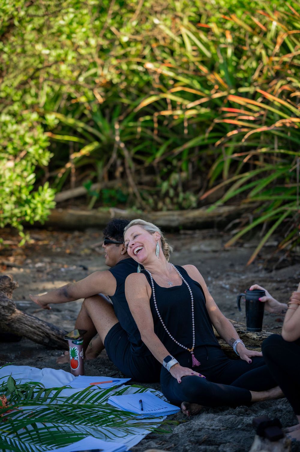 Person relaxing and laughing while lying down on a beach blanket next to tropical foliage.