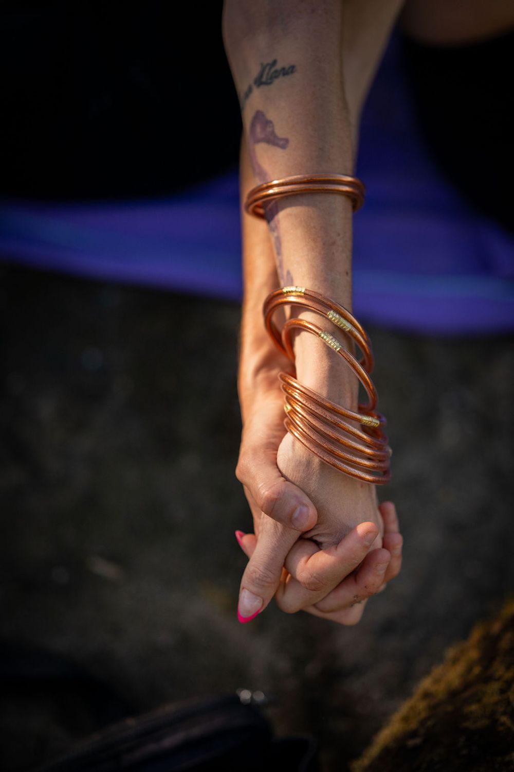 Close-up of a hand adorned with copper spiral bracelets against a dark background with a blue glow.