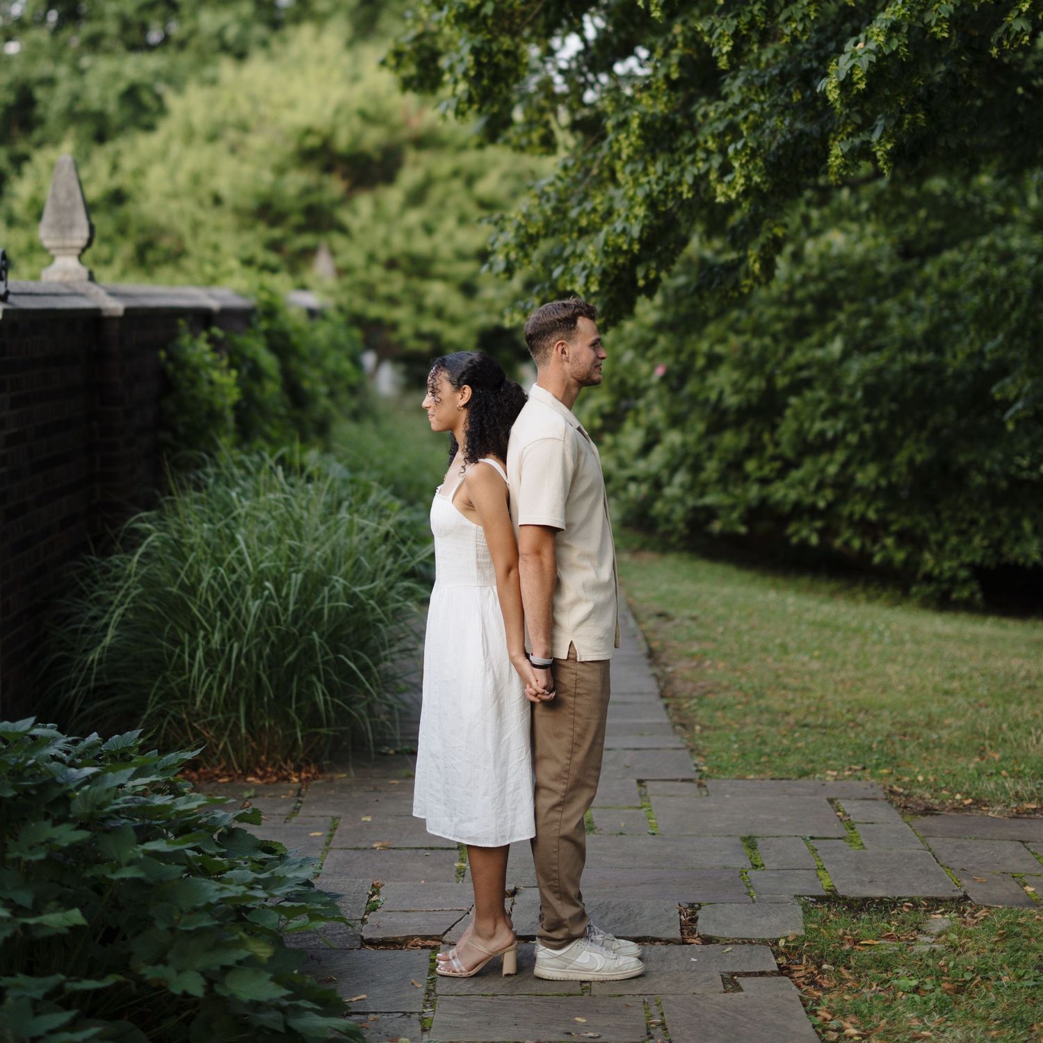 A couple shares a romantic moment while sitting on stone steps in a lush garden setting.