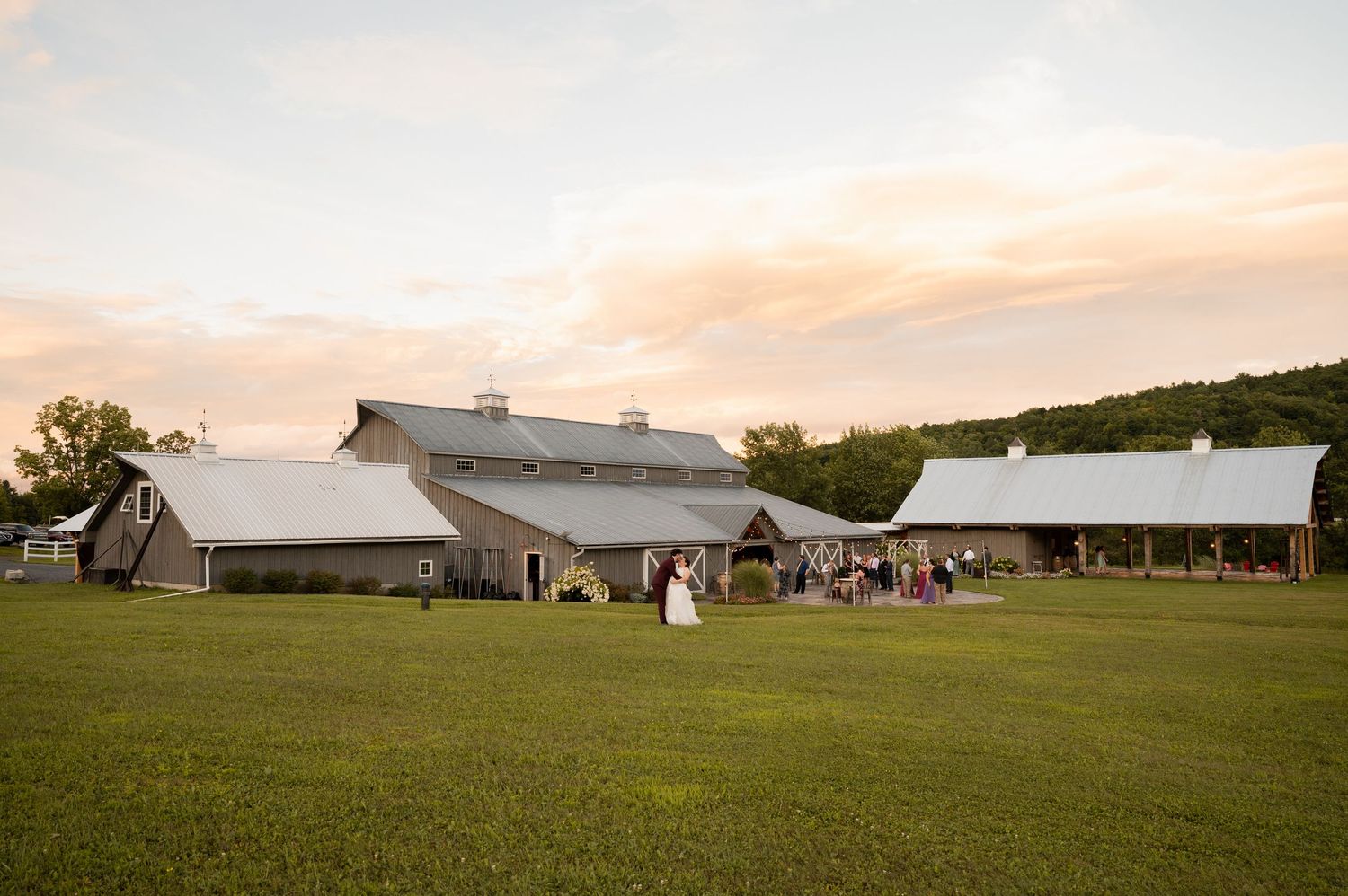 Large white wedding tents set up on a grassy field at sunset with warm golden sky overhead.