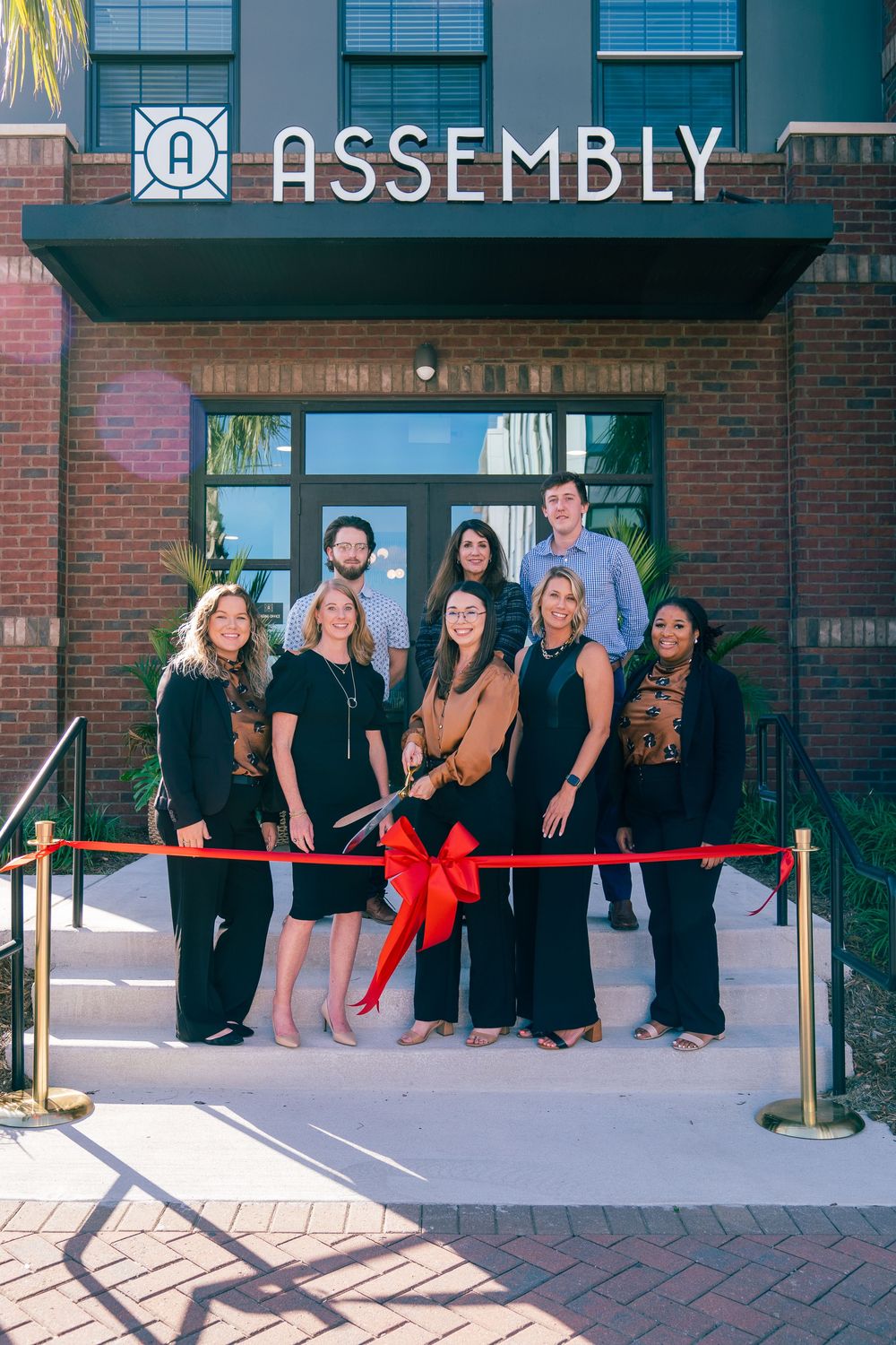 Group in black attire gathered for ribbon cutting ceremony at Assembly storefront.