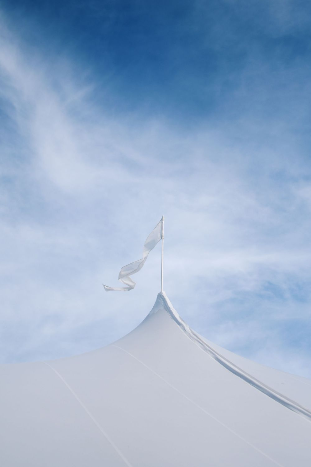 White event tent peak against blue sky with flag waving in the breeze.