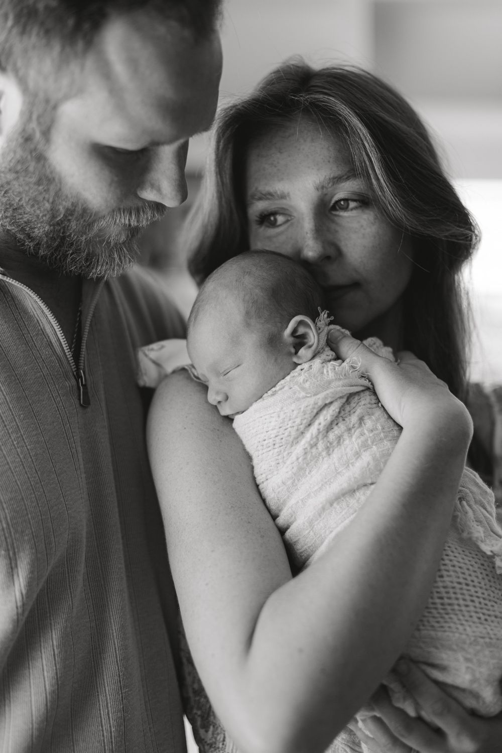 A tender black and white portrait of parents holding their sleeping newborn baby in an intimate family moment.