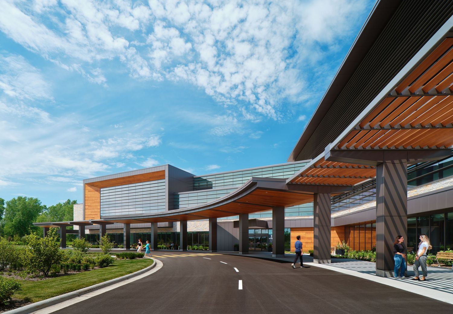 Modern healthcare building exterior with wooden pergolas and curved driveway under blue skies with white puffy clouds.