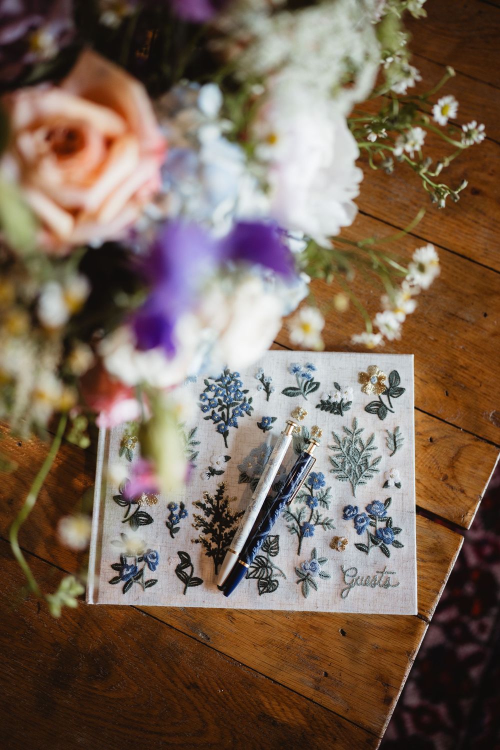 Decorative blue floral stamps and designs on a white paper with soft purple flowers in background on wooden surface.