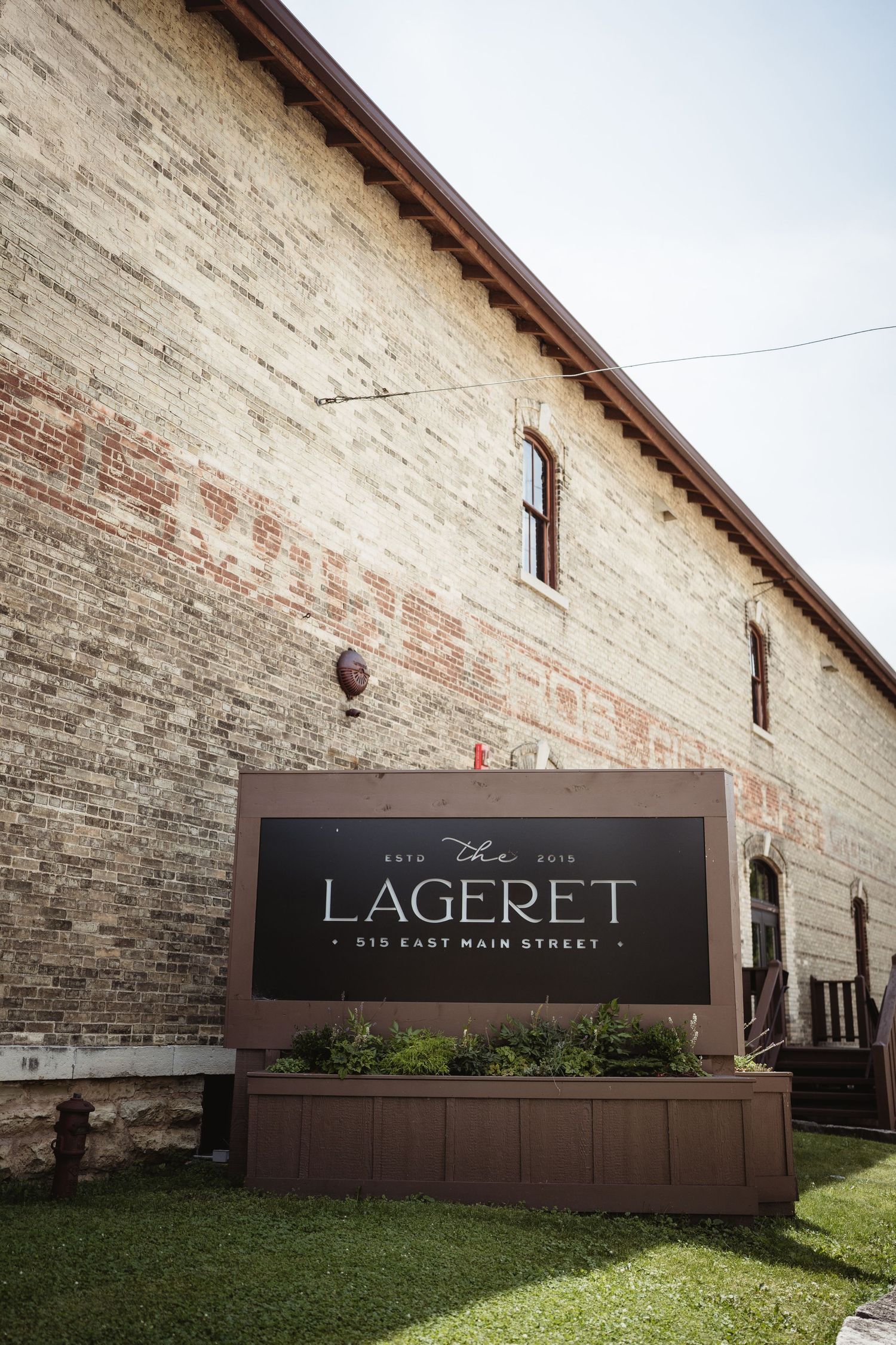 Exterior view of The Lagerret building with a rustic brick facade and wooden sign display on grassy lawn.