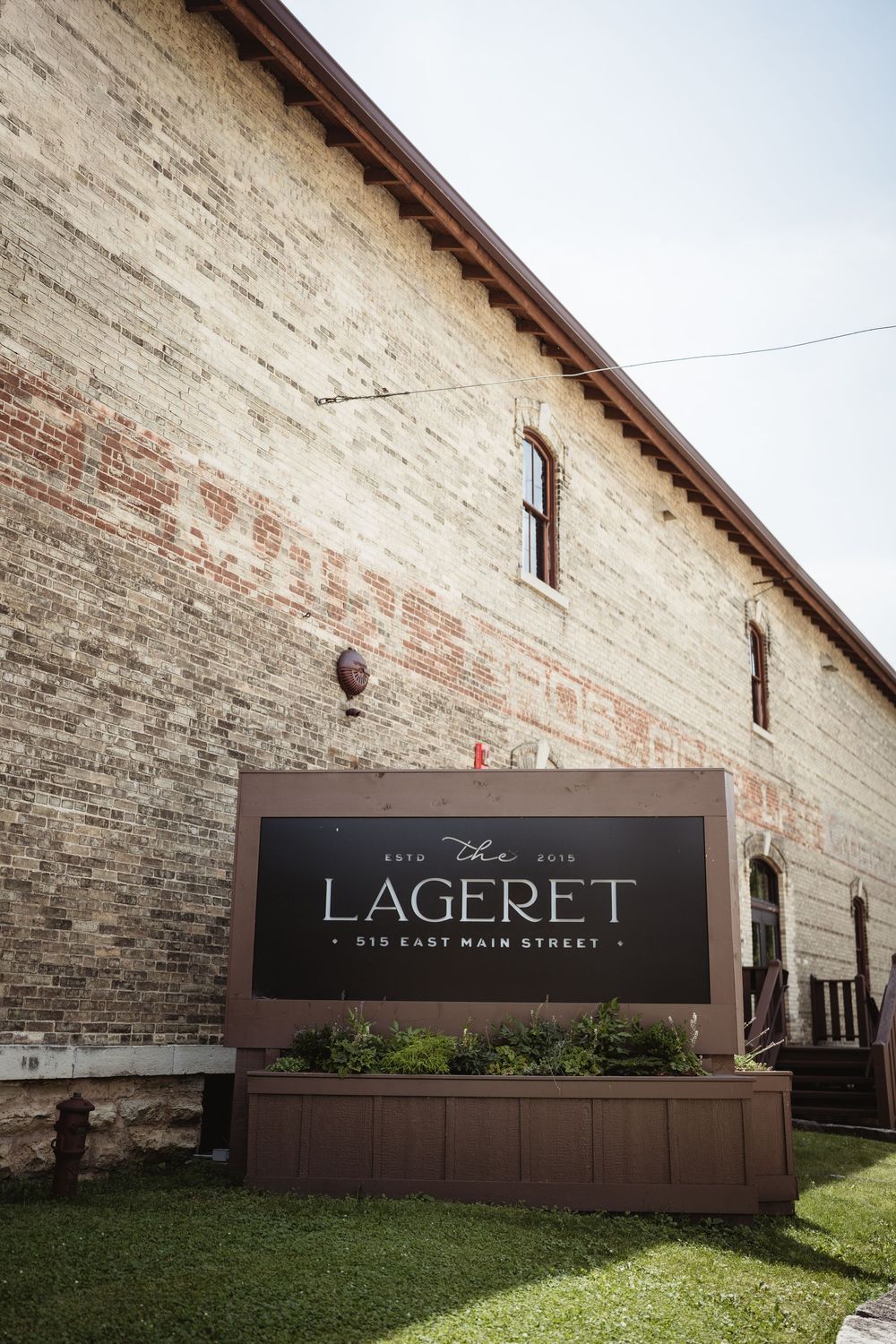 Exterior view of The Lagerret building with a rustic brick facade and wooden sign display on grassy lawn.