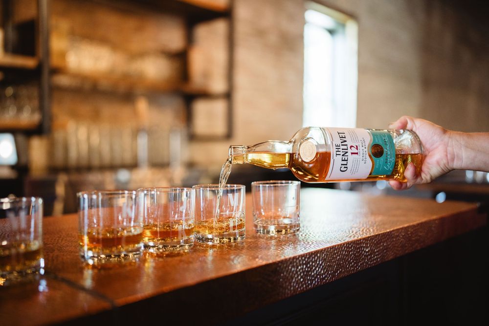 Bourbon being poured into multiple glasses at a wooden bar setup for tasting.