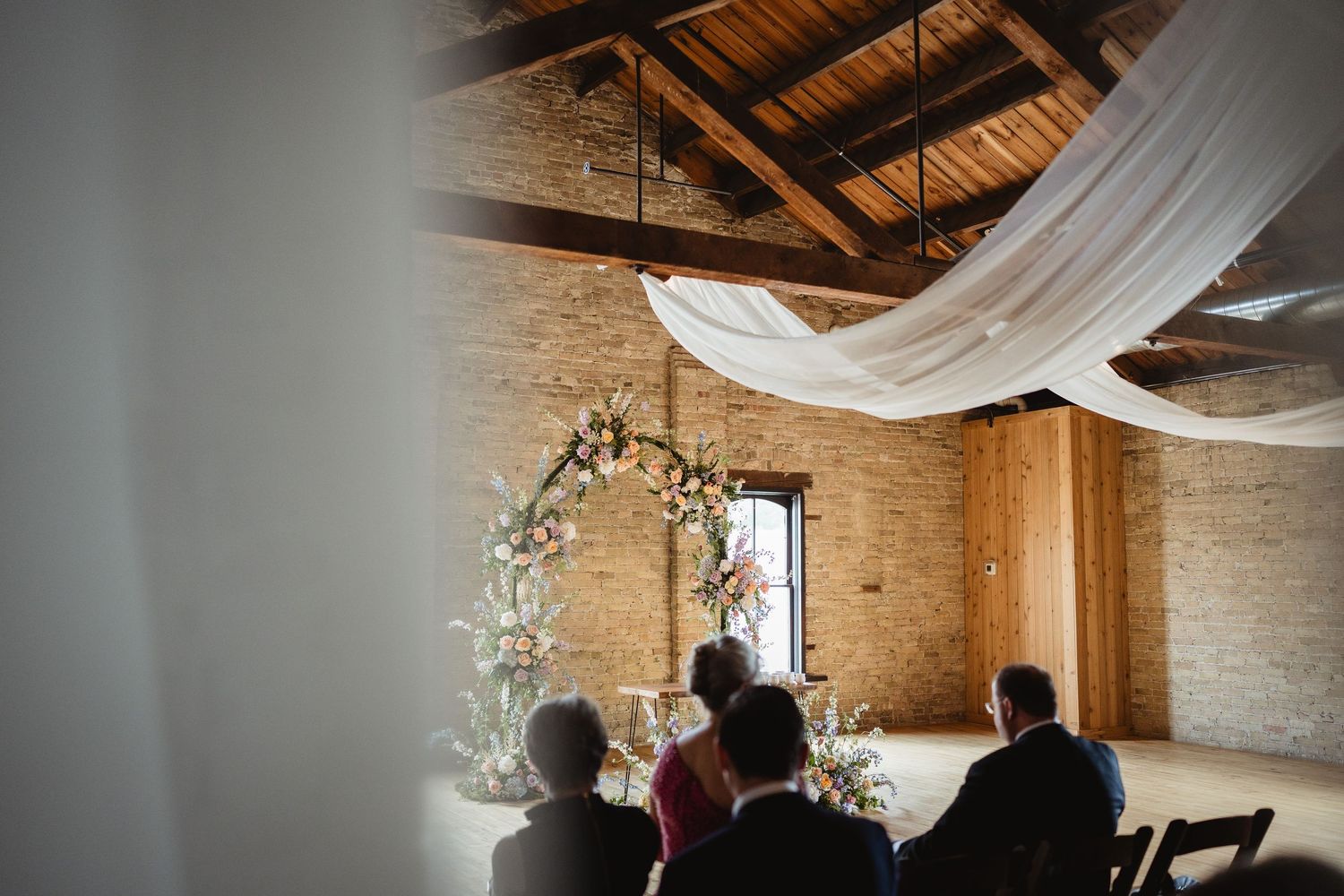Elegant rustic barn venue interior decorated with white fabric draping and florals for a wedding celebration.