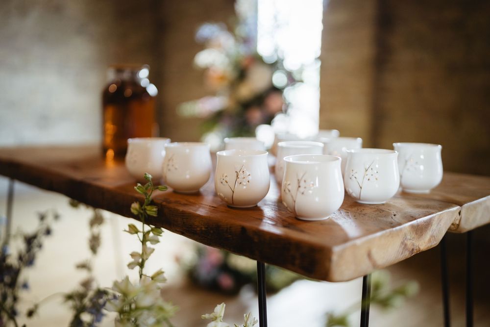 Row of white ceramic mason jar style candle holders arranged on wooden shelf with decorative greenery.