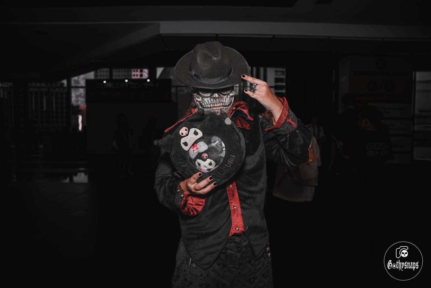 A photographer in dark clothing holds up a professional camera in a dimly lit environment.
