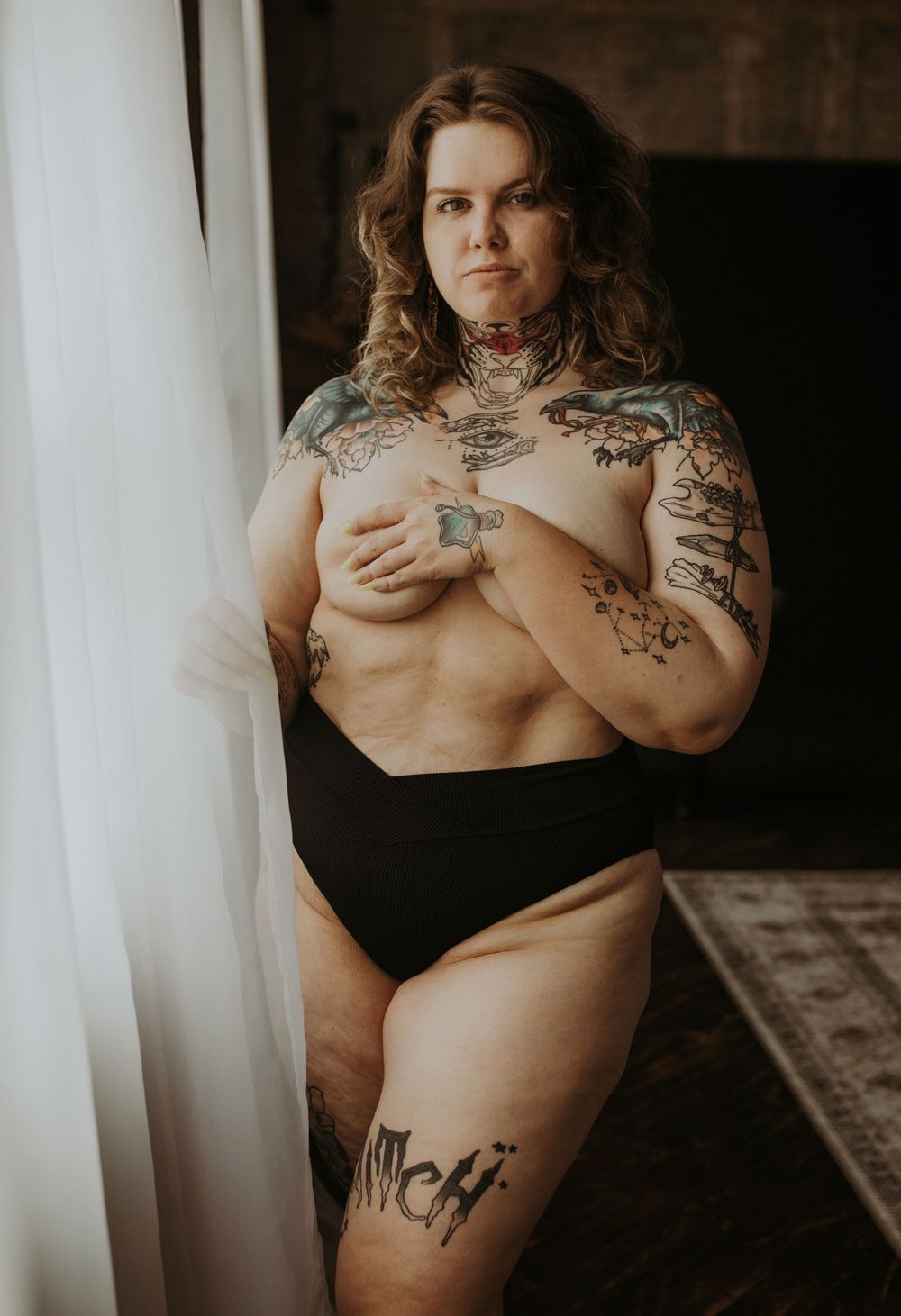 Artistic black and white boudoir photography showing a tattooed figure in intimate poses against white curtains.