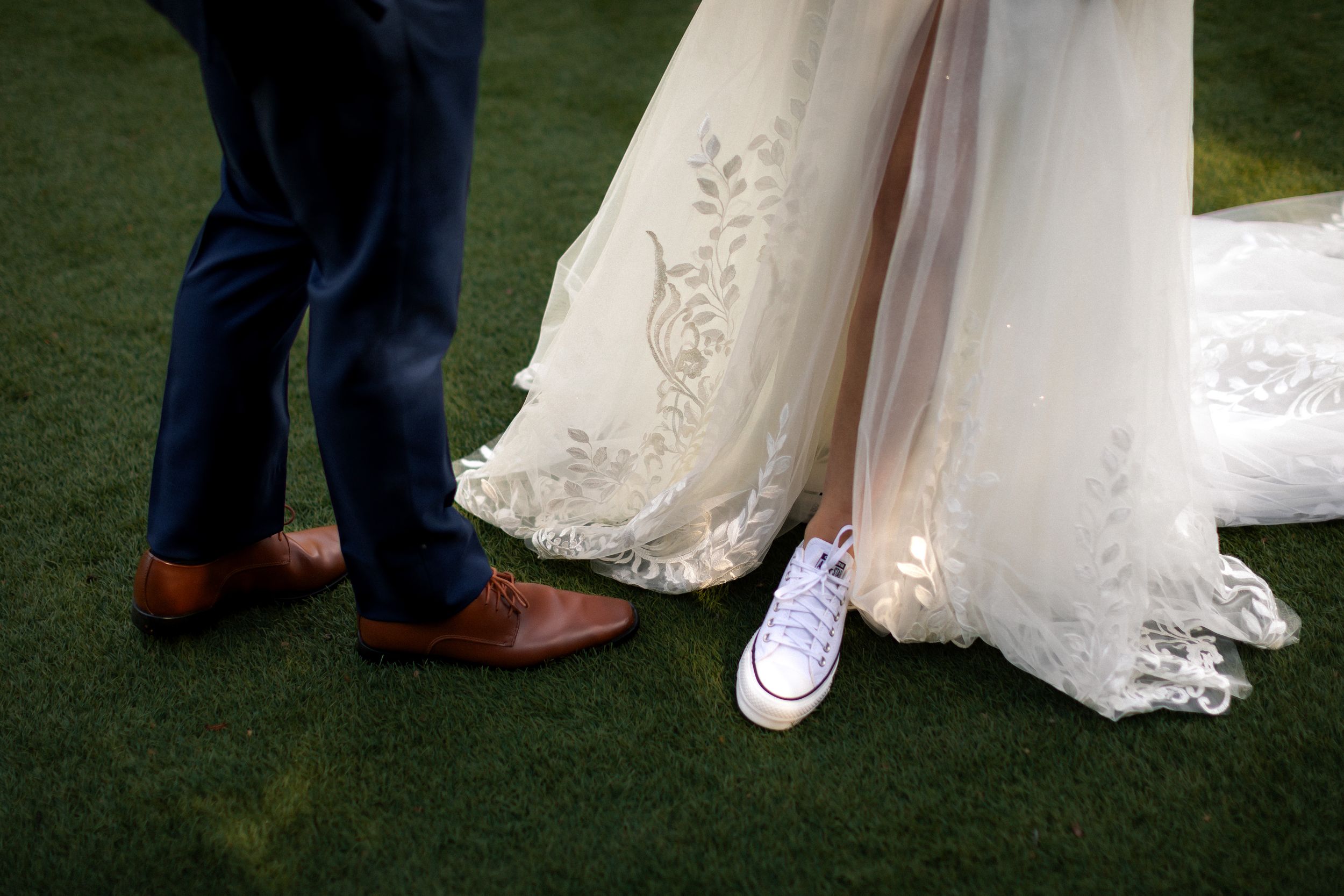 Wedding dress details showing lace trim and shoes against green grass.