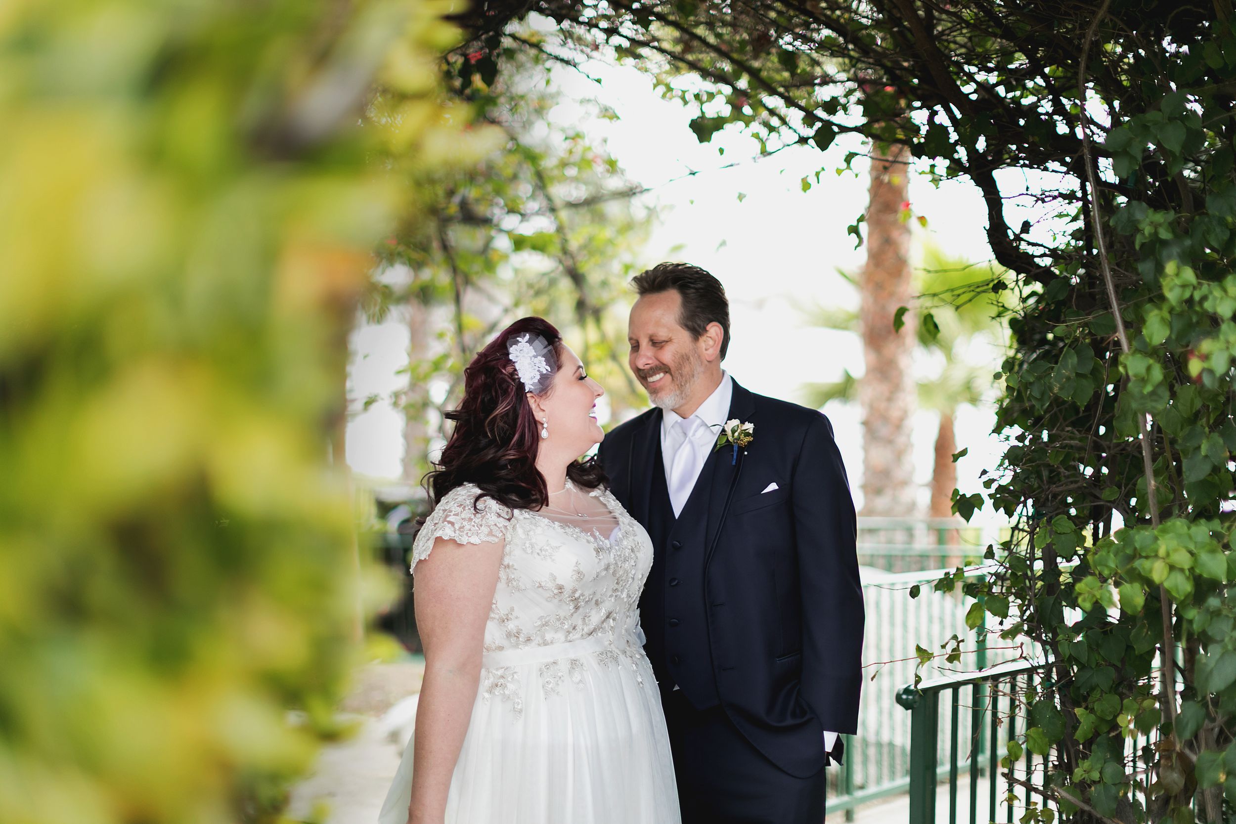 A wedding couple shares a loving moment under green foliage and natural lighting.