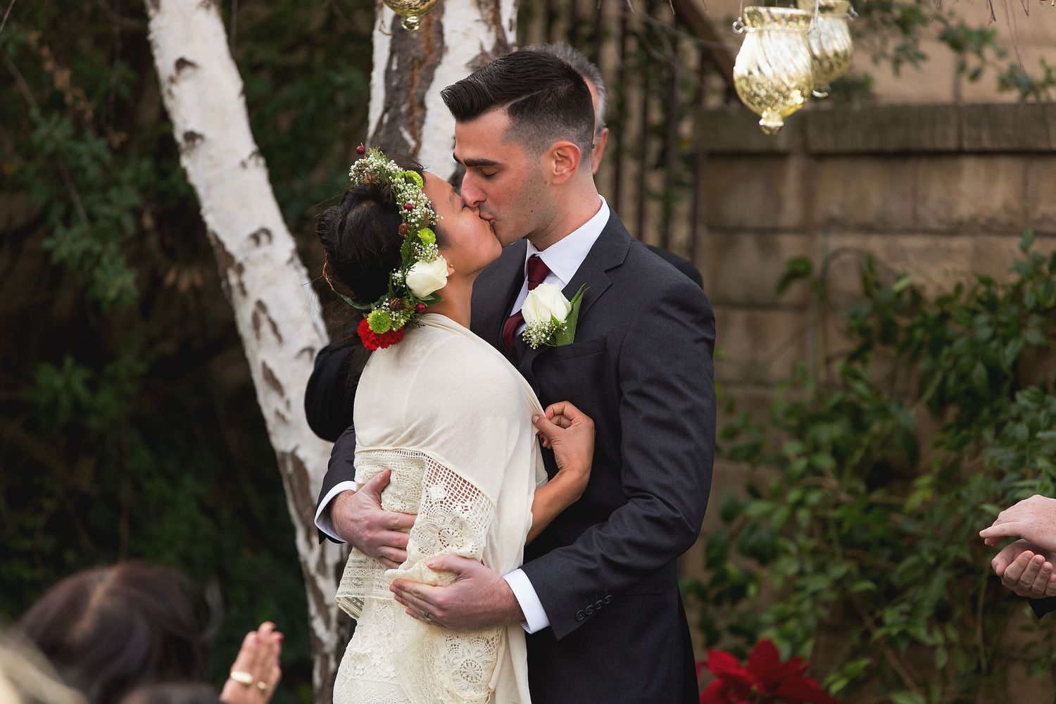 Intimate outdoor wedding ceremony beneath birch trees with lanterns hanging in the background.