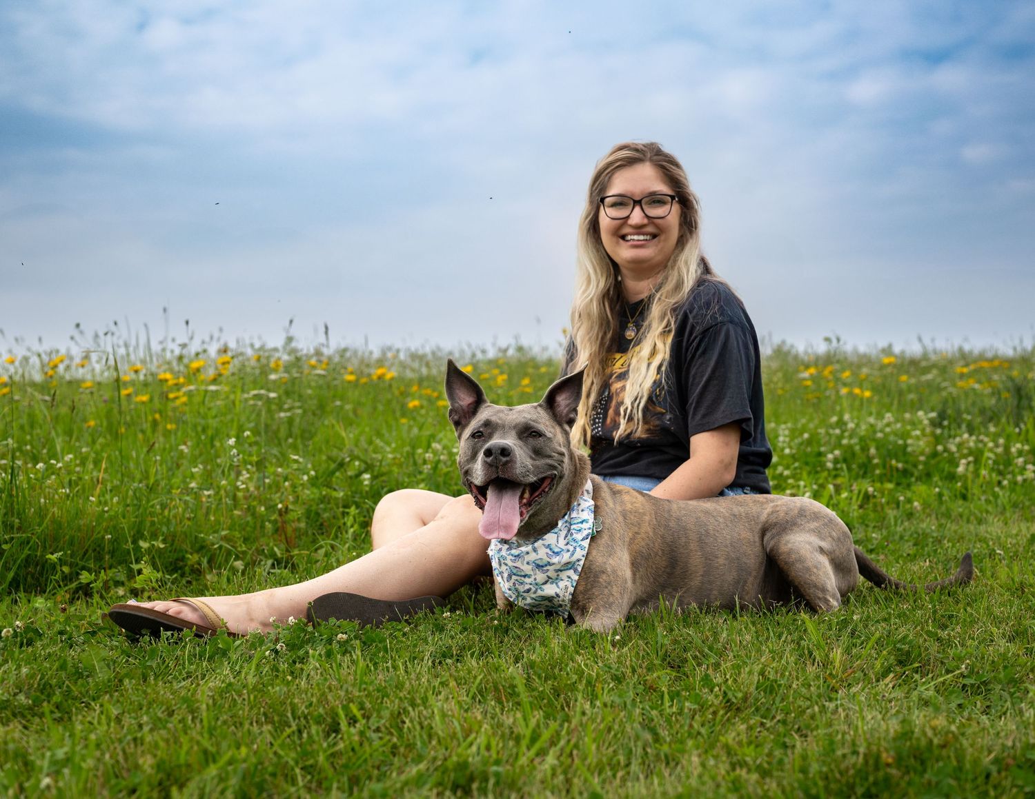 A young woman and her dog are sitting in a grassy field