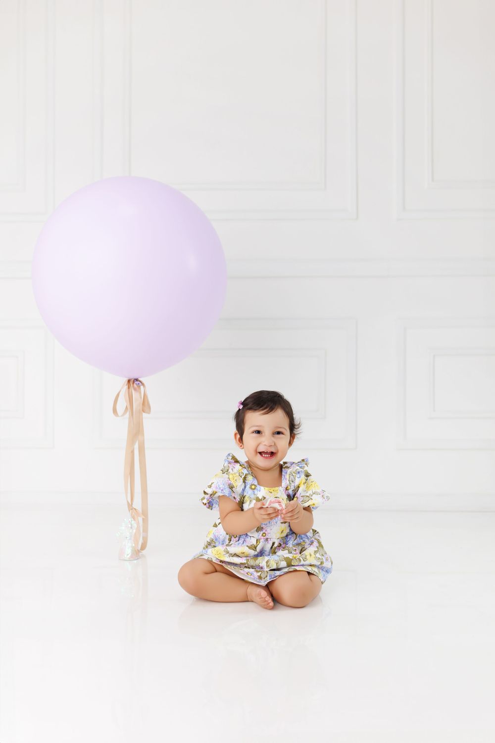 Baby portrait session with purple balloon in minimalist white studio setting.
