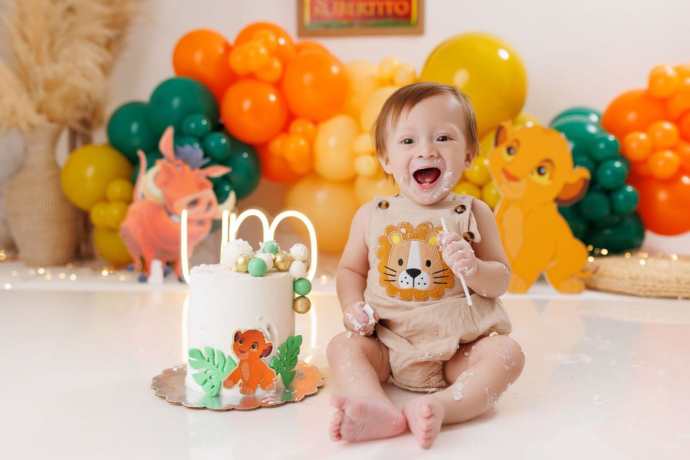 Baby's cake smash session with orange and yellow balloon arch and dinosaur decorations.