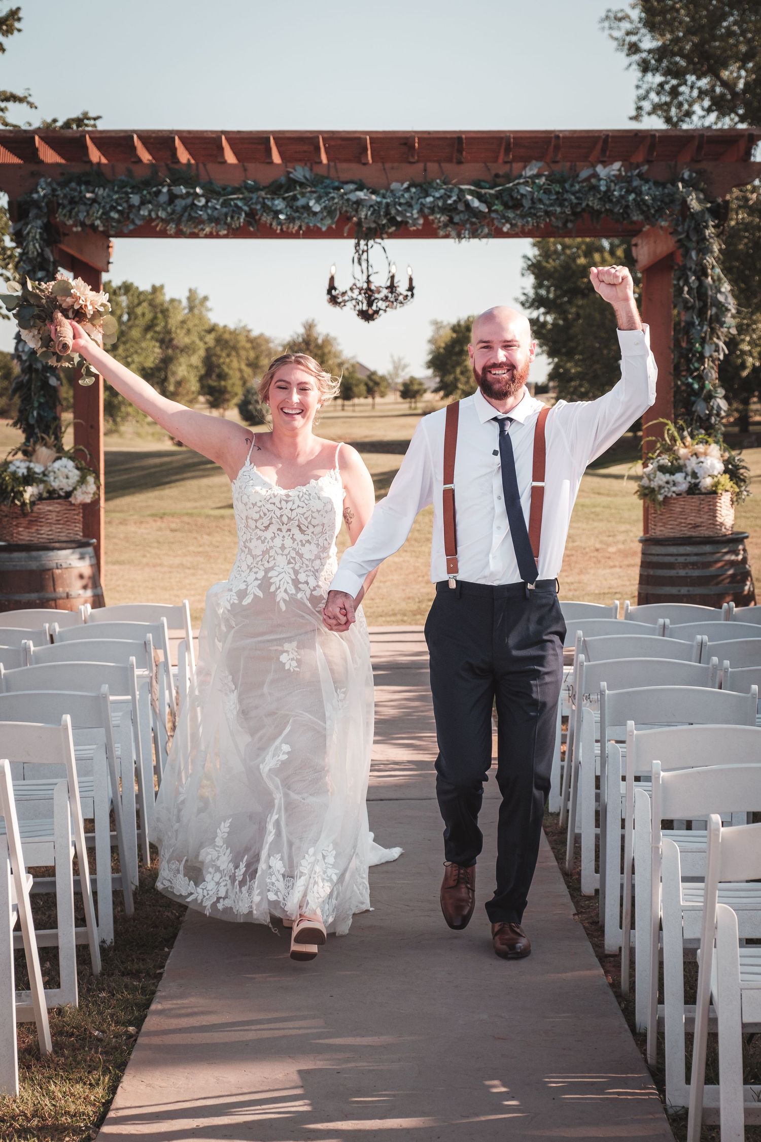 Newlyweds celebrating while walking down the aisle under a decorated outdoor ceremony arch.