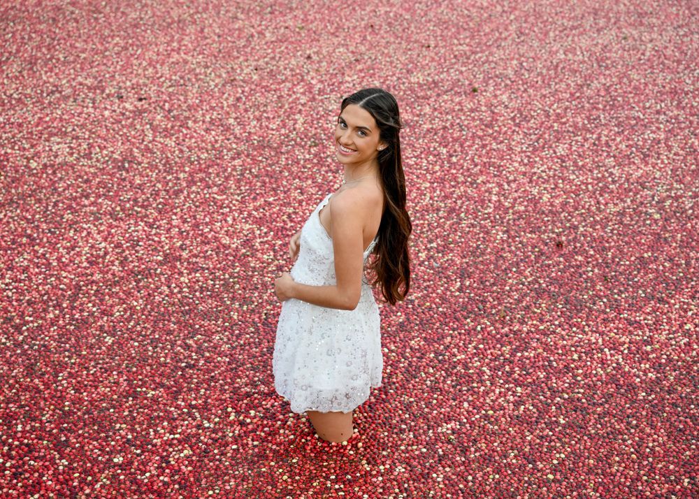 Young woman in white lace dress smiling while standing in a flooded red cranberry bog.