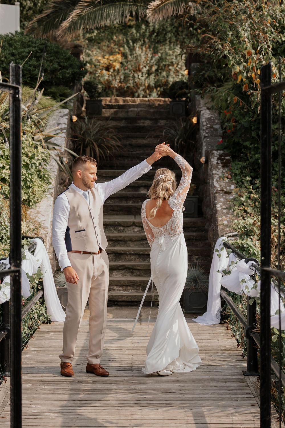 Bride and groom dancing on a wooden bridge surrounded by lush greenery at an outdoor wedding venue.