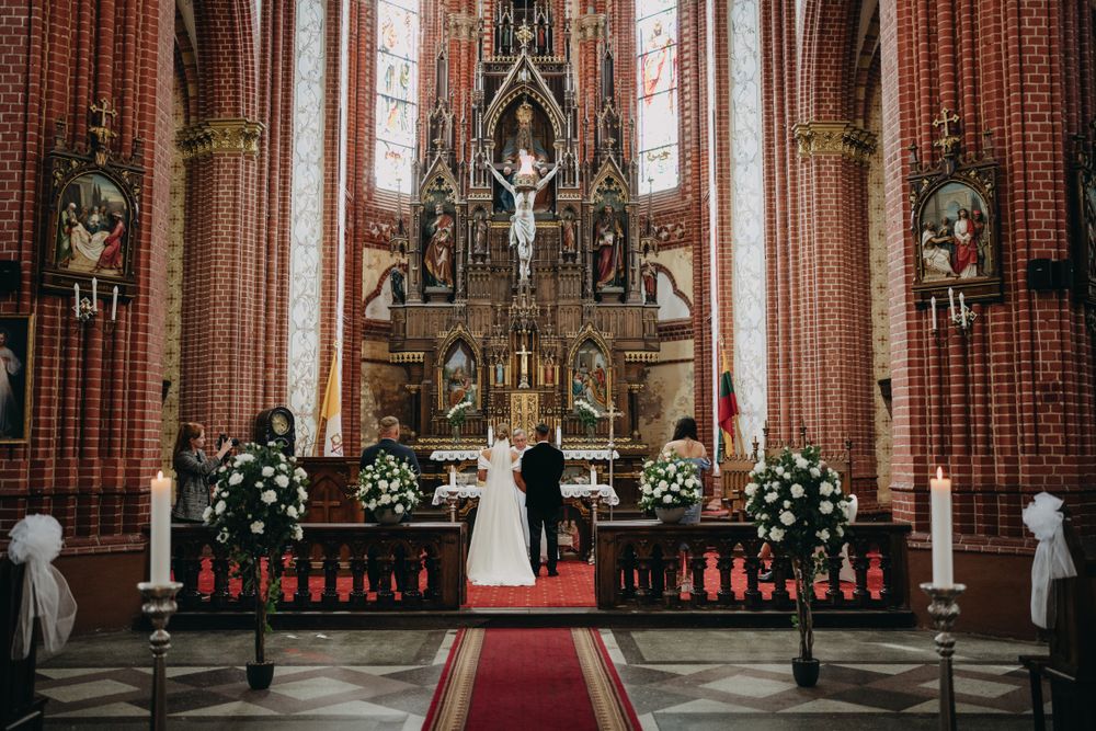 Interior of a grand gothic church with ornate altar, red carpet, and brick walls.