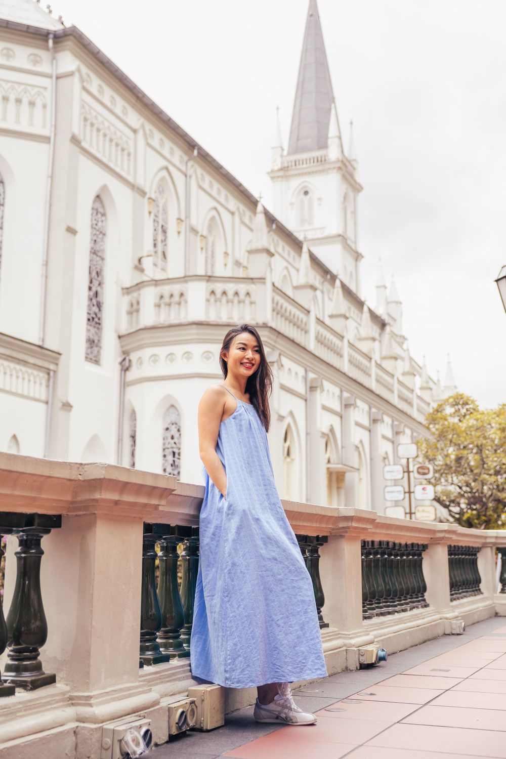A person in blue dress poses in front of white gothic church with tall spire.