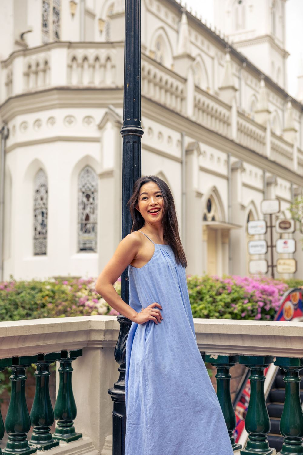 Light blue sundress contrasts beautifully against gothic church architecture with ornate details and pink flowers.