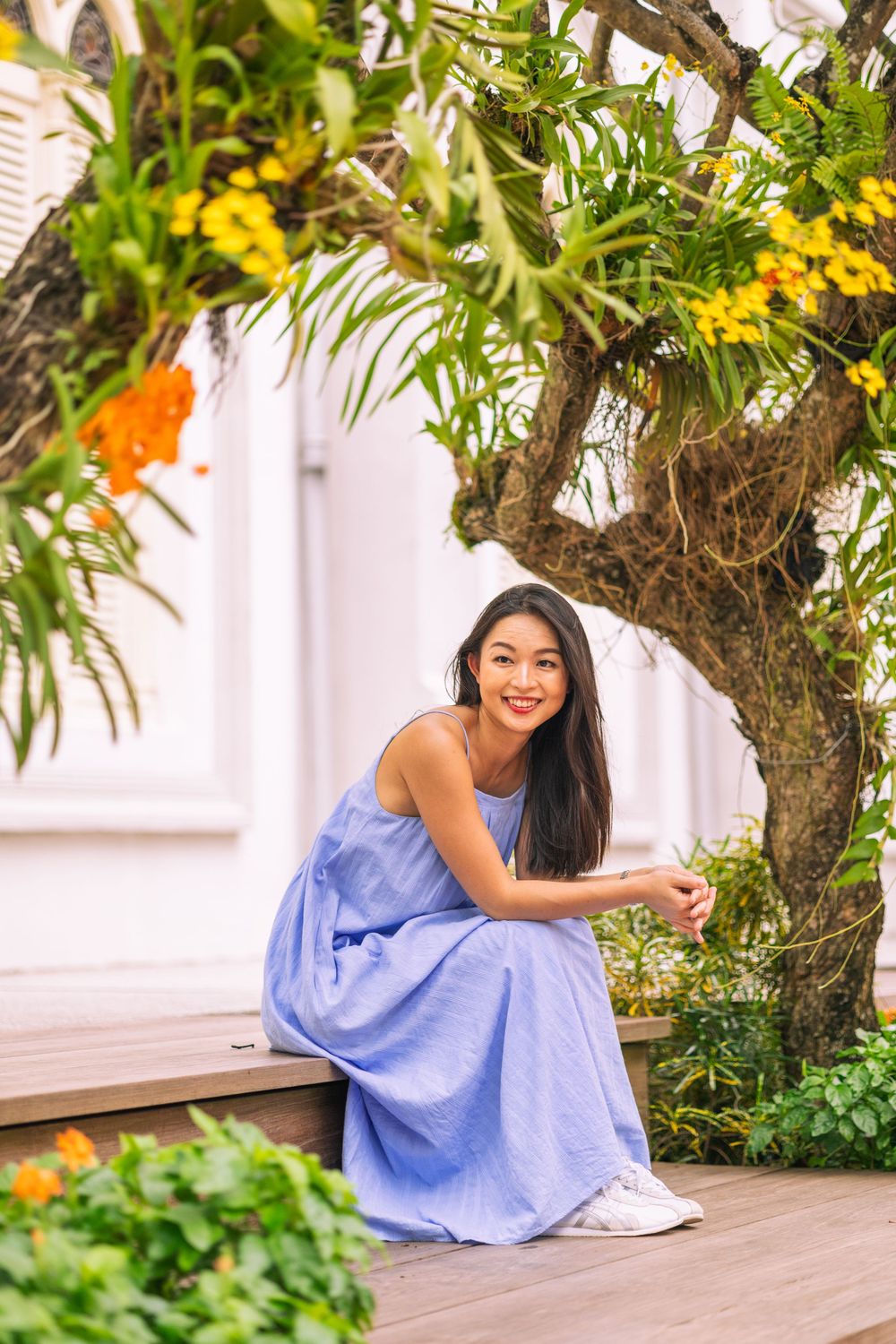 Summer garden scene with blue dress framed by yellow flowers and tropical foliage.