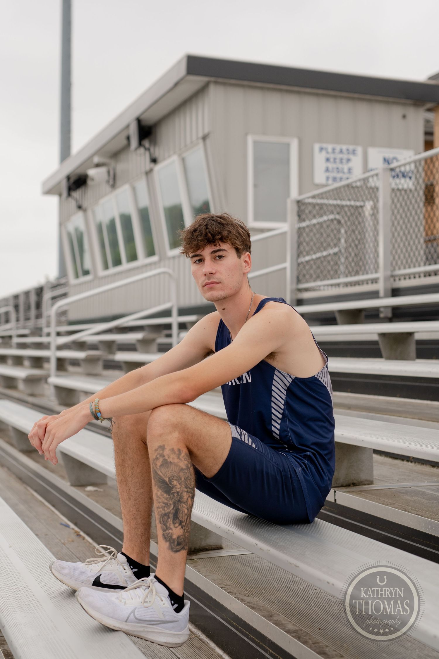 Student athlete in navy uniform sits on bleachers showing leg tattoo.