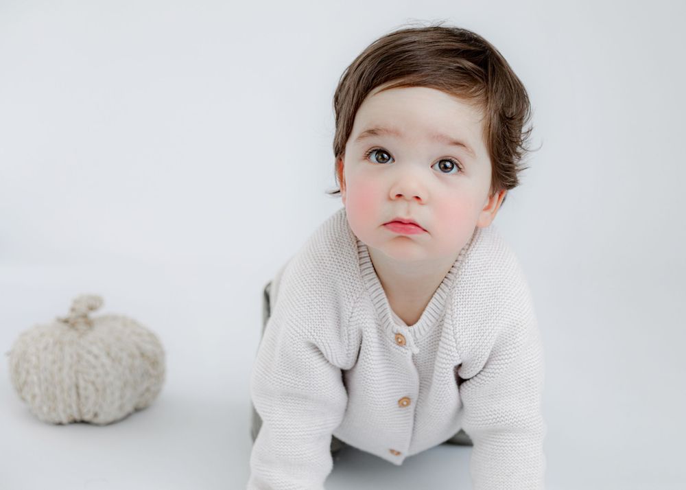 Close up portrait of child in cream cardigan with decorative pumpkin in background.