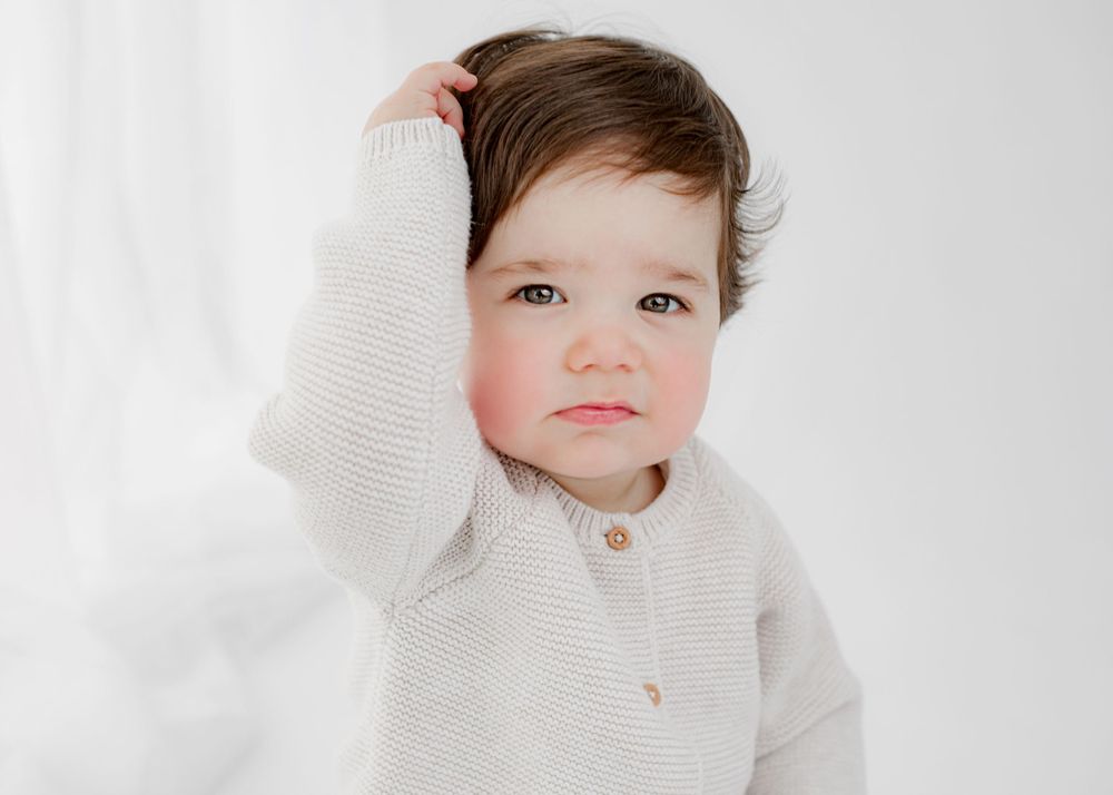 Young child wearing cream cardigan sweater against white background.