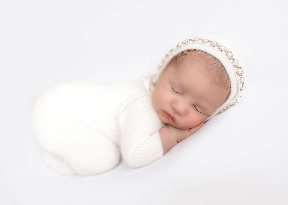 Peaceful sleeping newborn wrapped in white with delicate pearl headpiece.