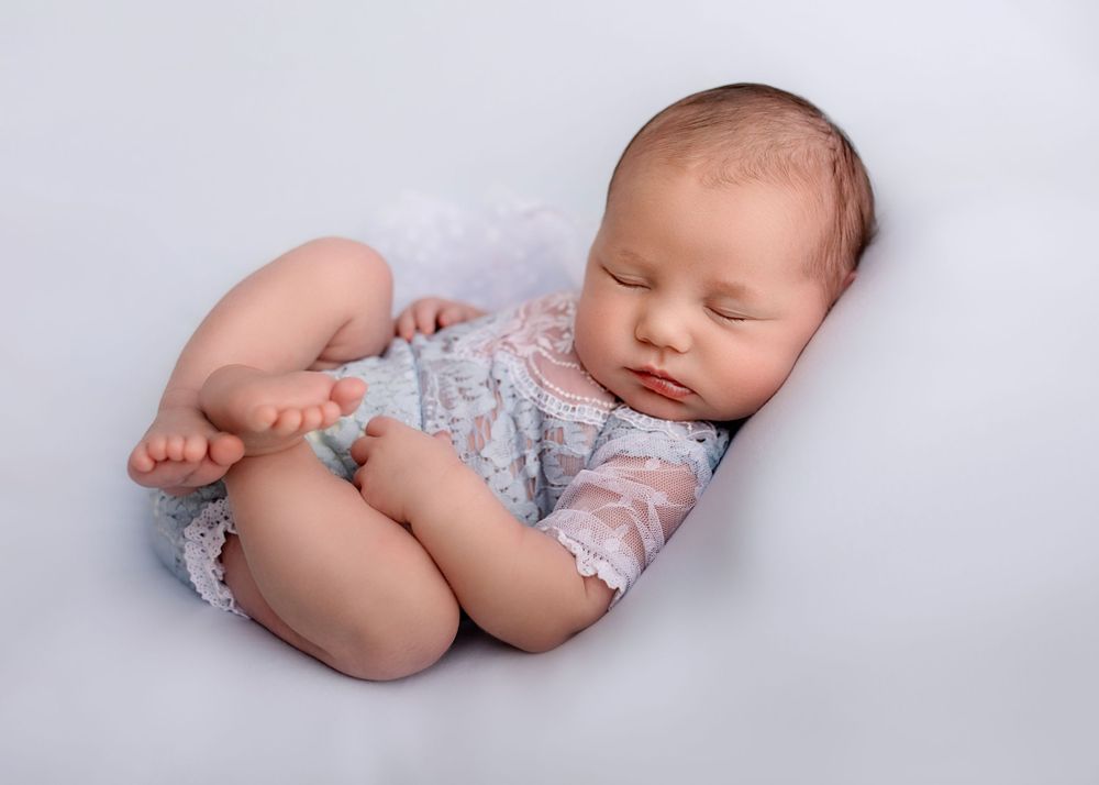 Sleeping infant in floral outfit rests peacefully on soft gray background.