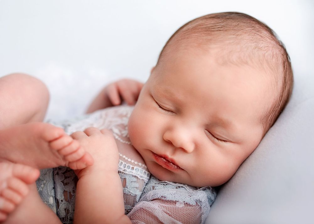Sleeping newborn in gray outfit with hand gently touching their foot during professional photo session.