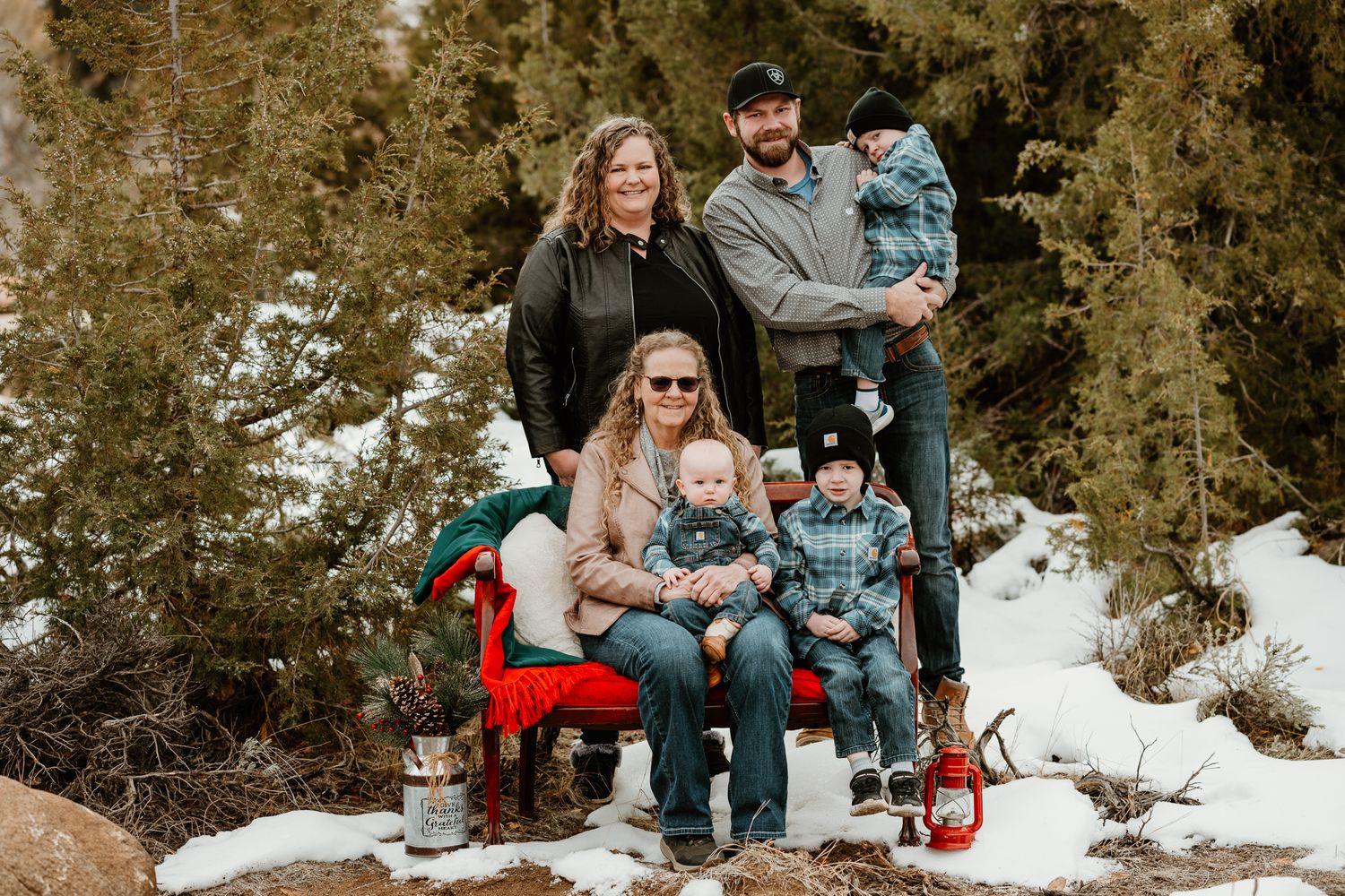 A family sits together on snowy ground with evergreen trees in the background.