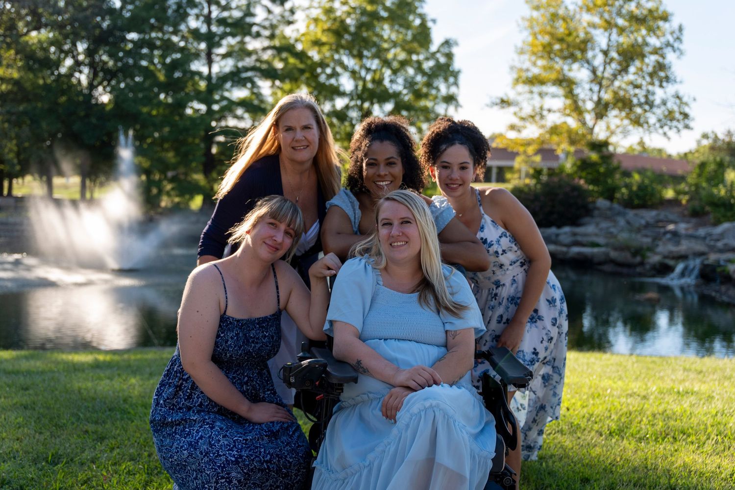 A group of friends pose together for a portrait by a scenic pond at sunset.