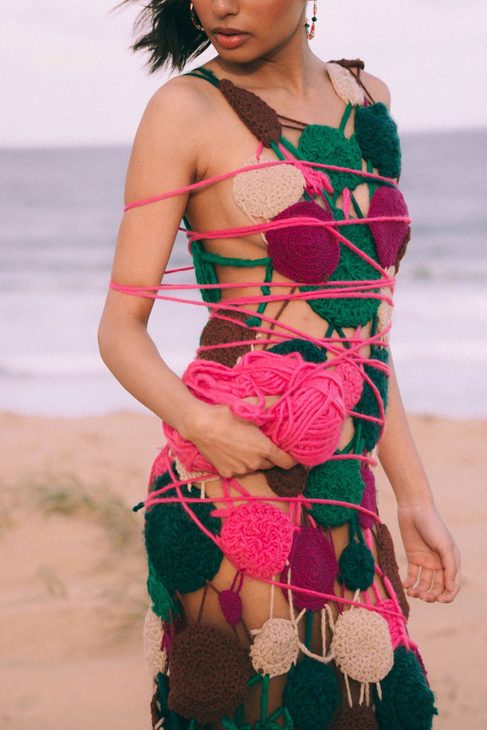 Close-up of artistic dress design featuring pink yarn and floral patterns against beach backdrop.
