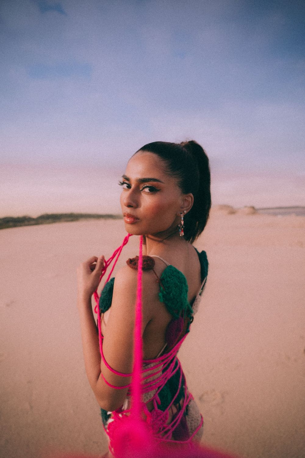 Artistic beach portrait with pink yarn elements against dusky desert background.