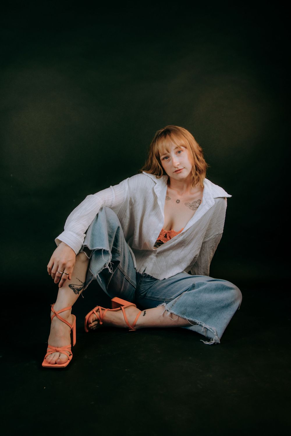 Artistic portrait showing relaxed pose on floor wearing white shirt and jeans.