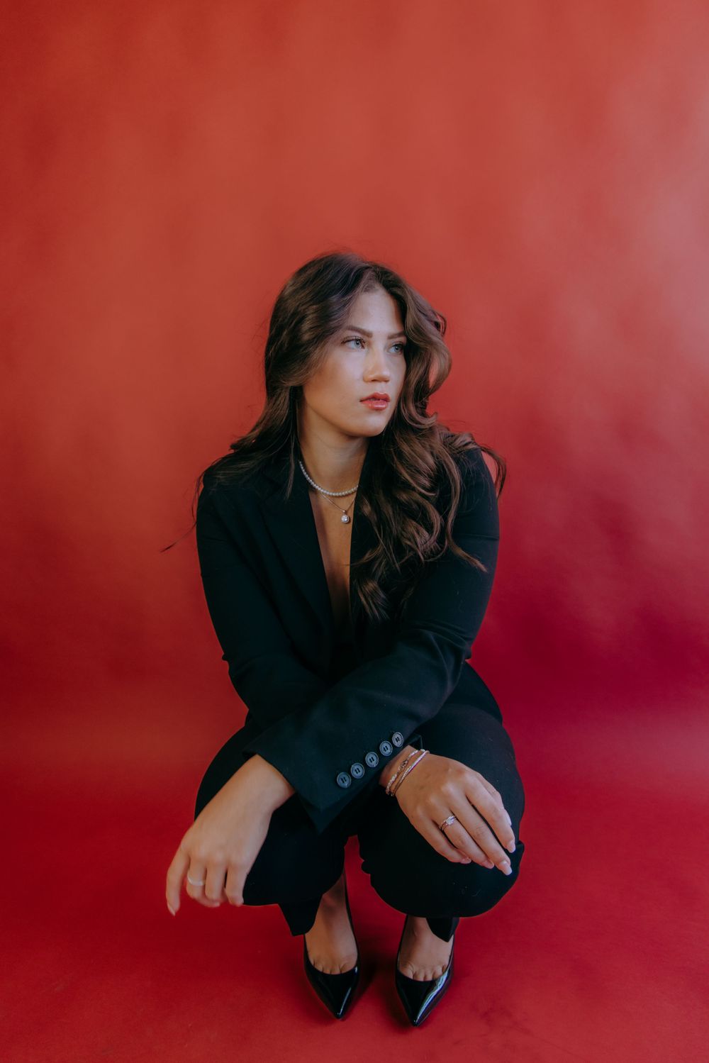 Fashion portraits against red backdrop featuring crouching poses in all-black ensemble.