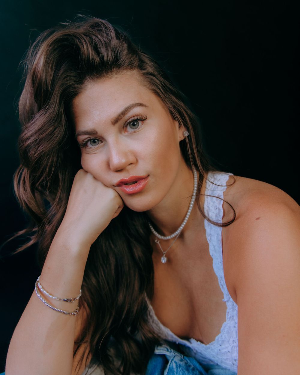Close-up fashion portrait with white top and jewelry against dark background.