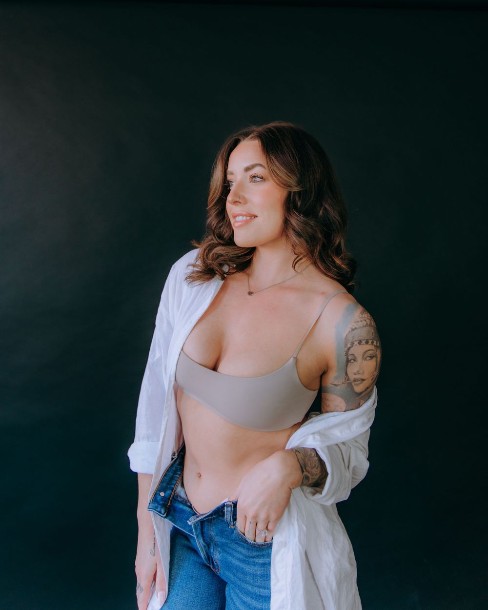 Studio fashion photo featuring relaxed pose in casual wear against dark background.