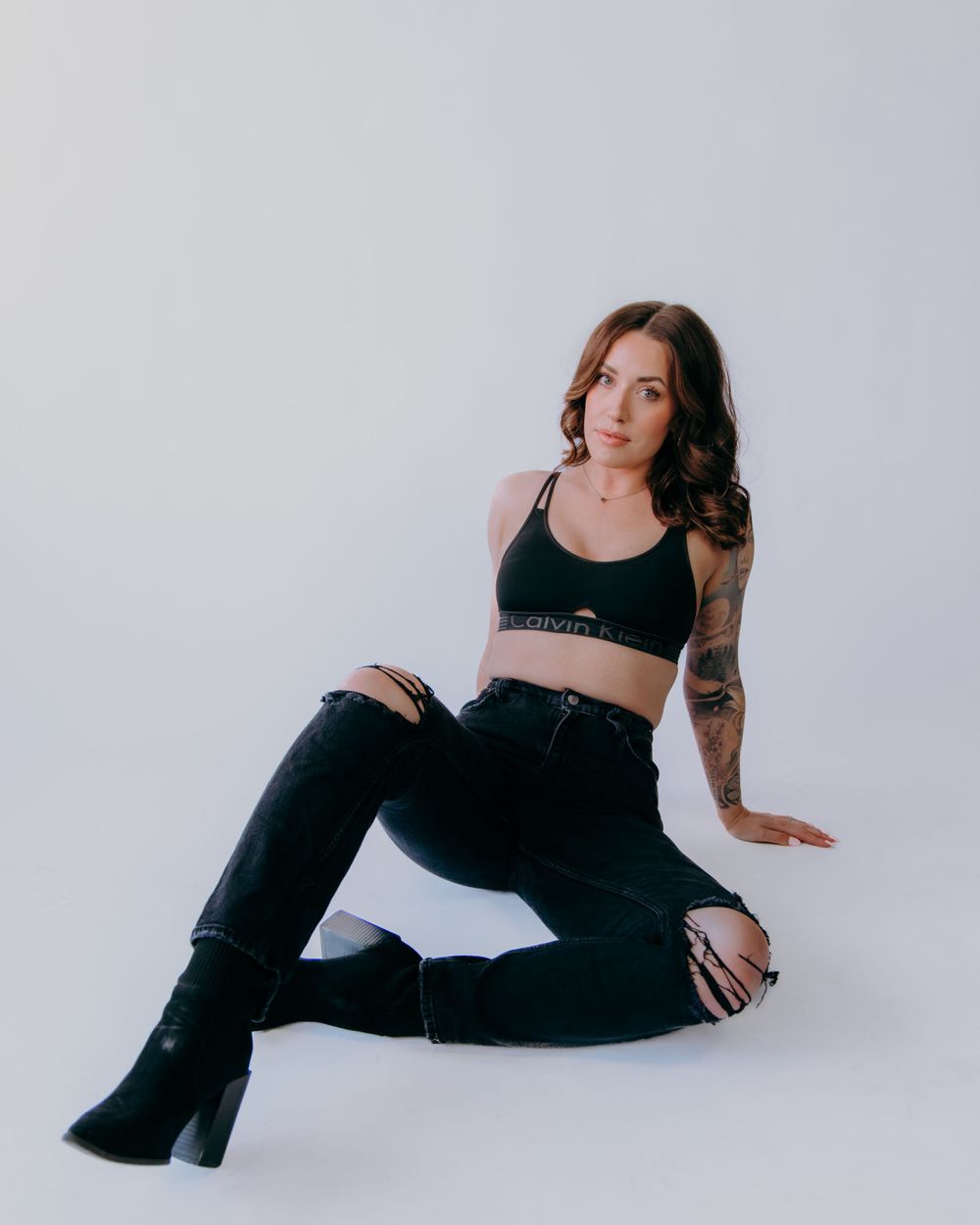 Reclining fashion pose in black ensemble against white studio backdrop.
