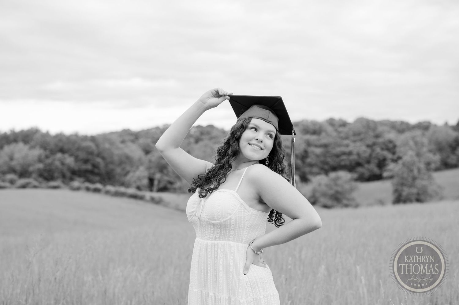 Black and white graduation photo of graduate posing playfully in a field.