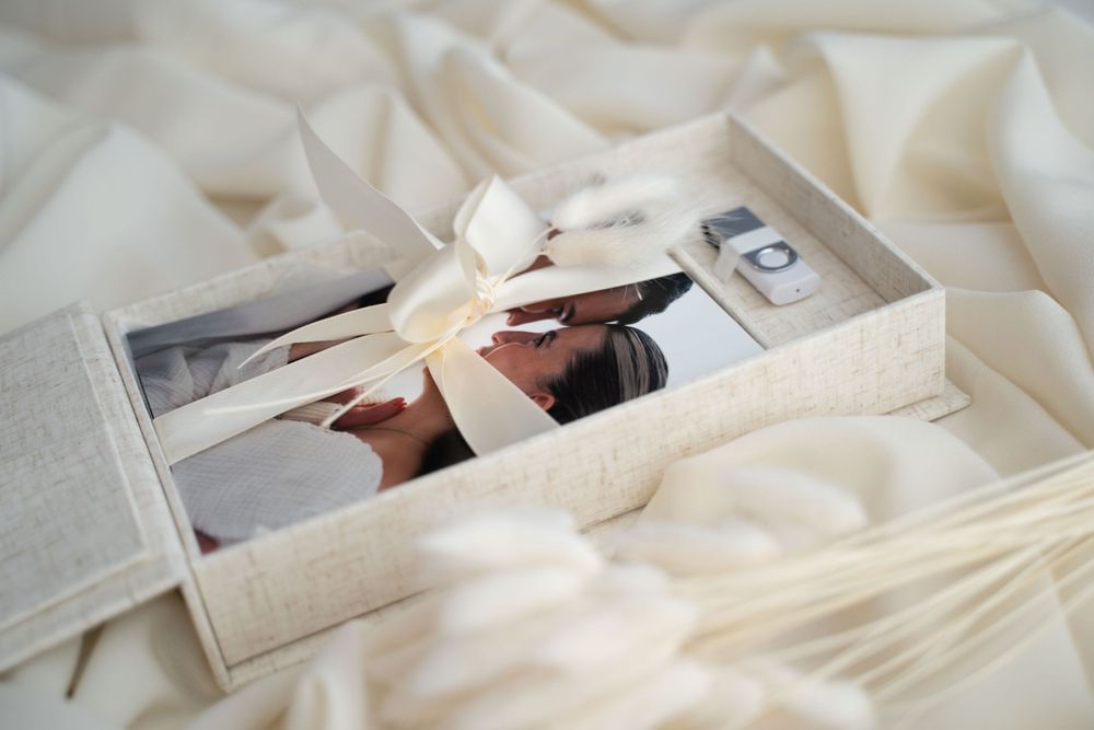 Elegant photo box with ribbon bow containing printed photos and USB drive on white silk fabric.