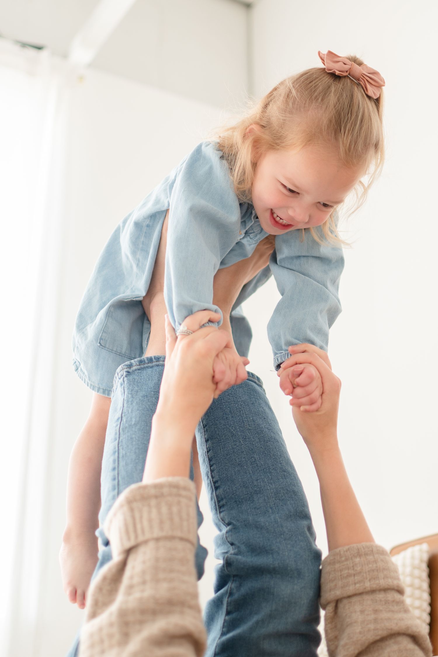 Child being lifted in air wearing denim outfit with joyful expression.