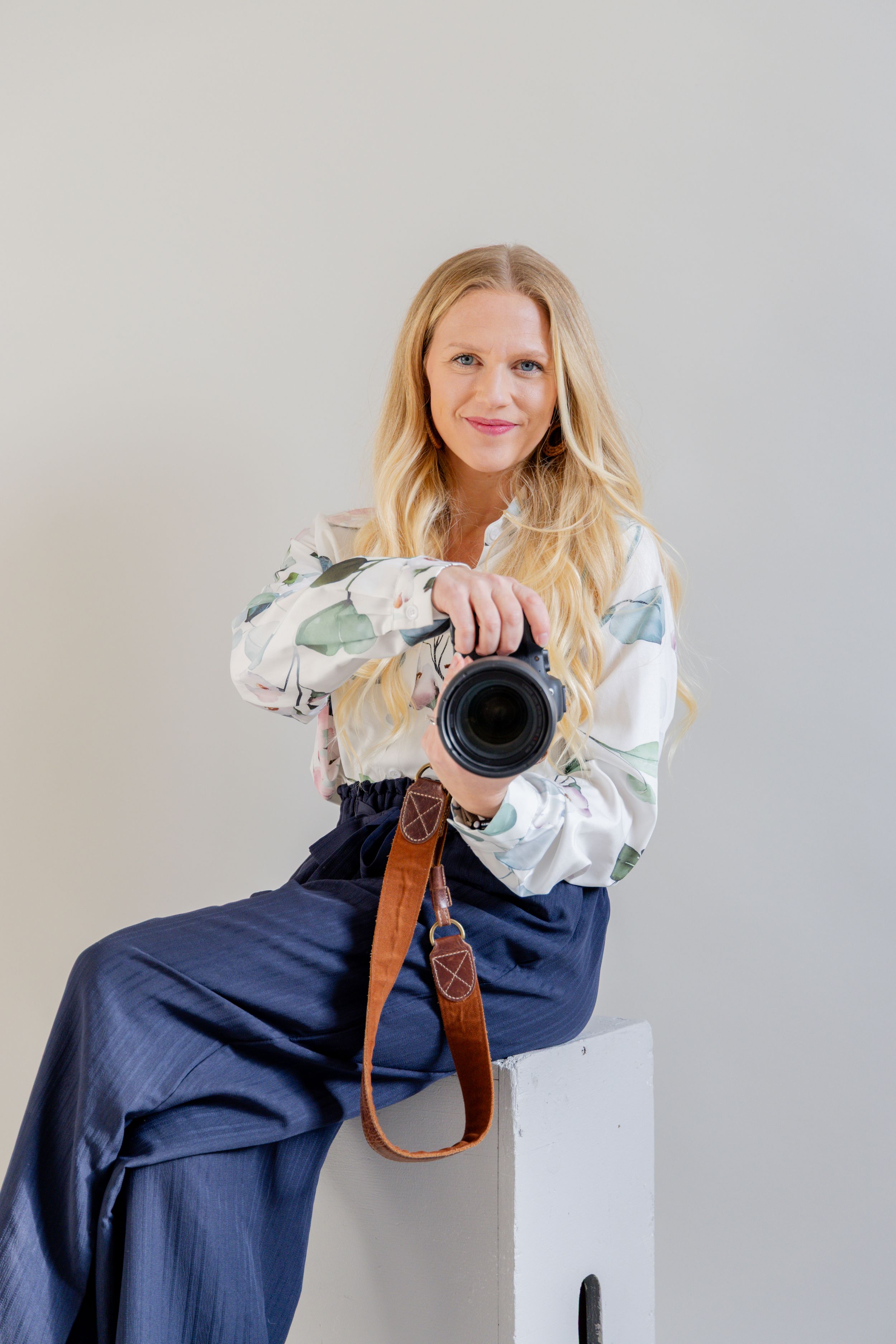 Minnesota professional photographer Maegan, sitting in a white studio holding a Canon camera, showcasing a behind-the-scenes look.