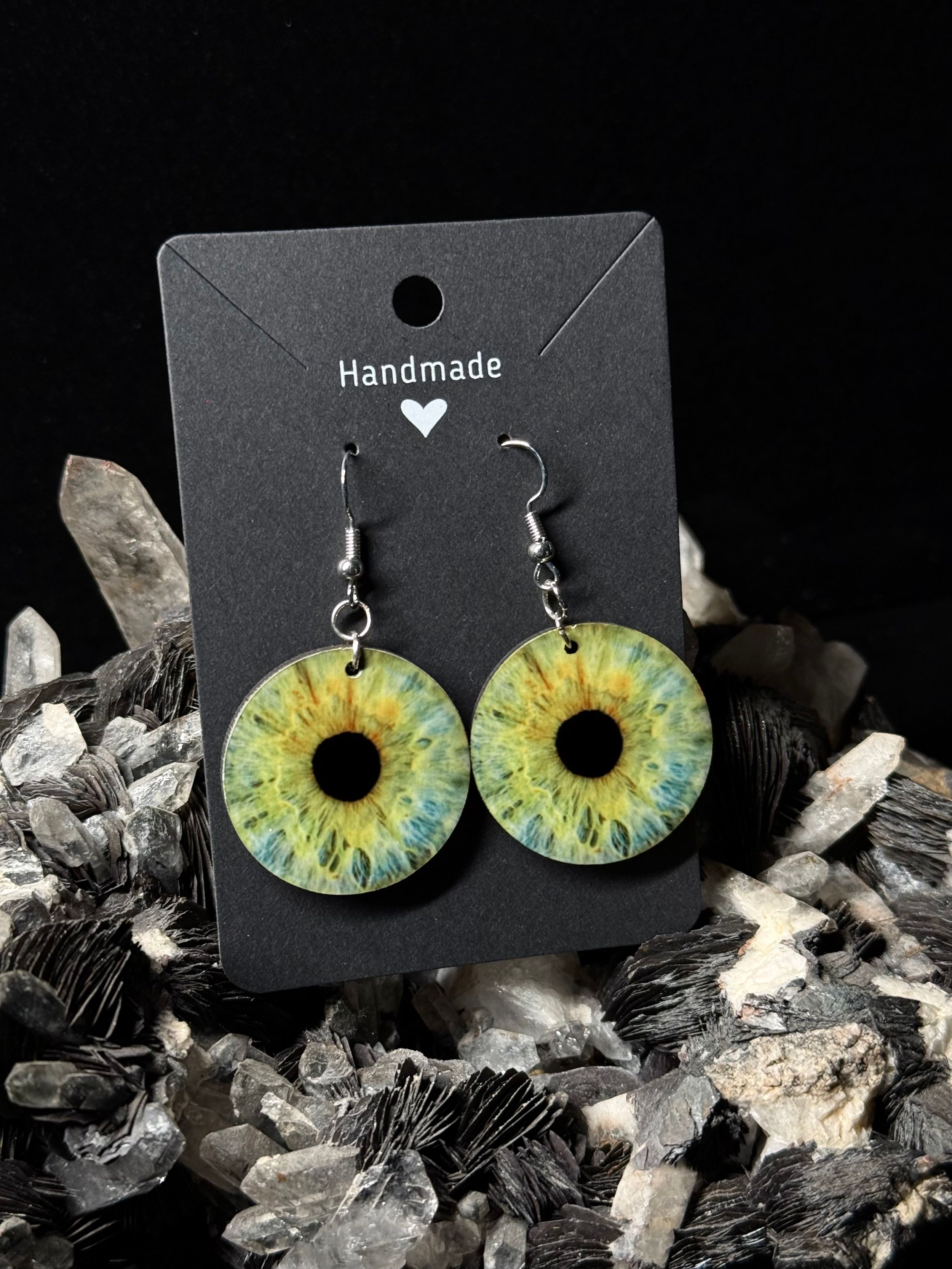 Handmade green and blue iris-styled earrings displayed on a black card against crystal minerals background.