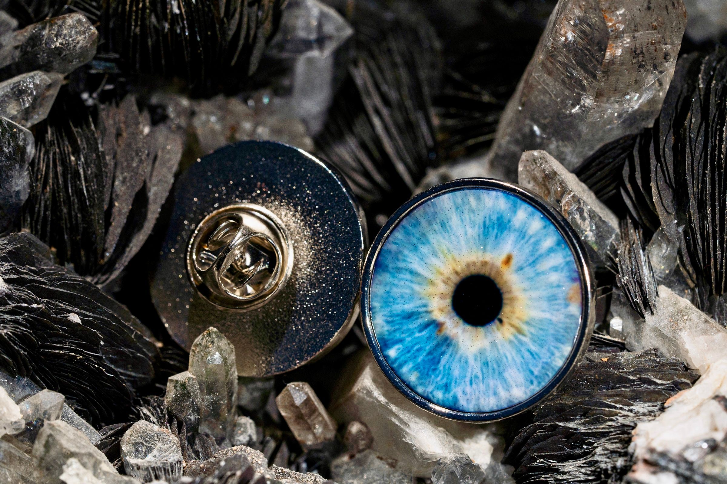 Two glass eye prosthetics, one black and gold mechanical style and one bright blue realistic iris, rest among crystals.